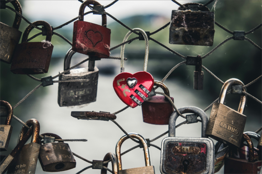 Rotes Herzschloss mit Aufschrift "The Kiss" zwischen Vorhängeschlössern- Symbol für Liebe und Genuss.